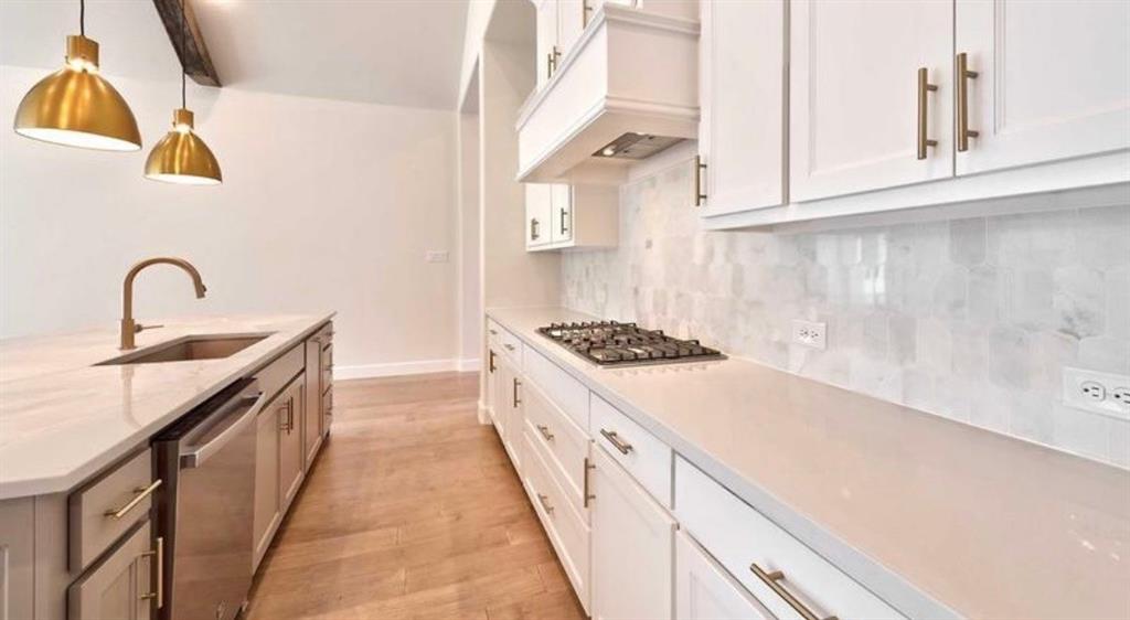 Kitchen featuring white shaker cabinetry, stone-finish countertops, geometric tile backsplash, metallic pendant lighting, and wood-finish flooring