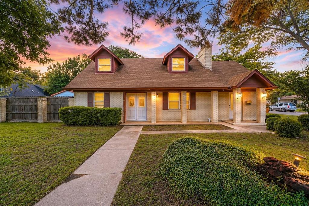 Brick exterior residence featuring a covered front porch, dual dormer windows, double-door entry, and a concrete walkway