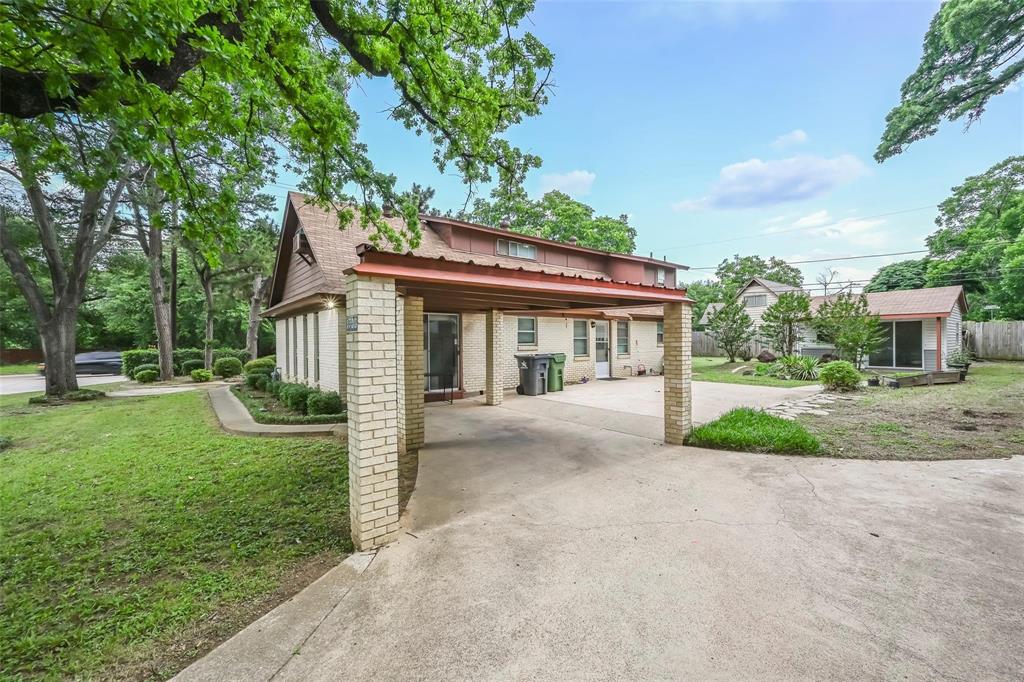 Exterior features include a covered carport with masonry support pillars, concrete driveway, brick facade, and mature landscaping