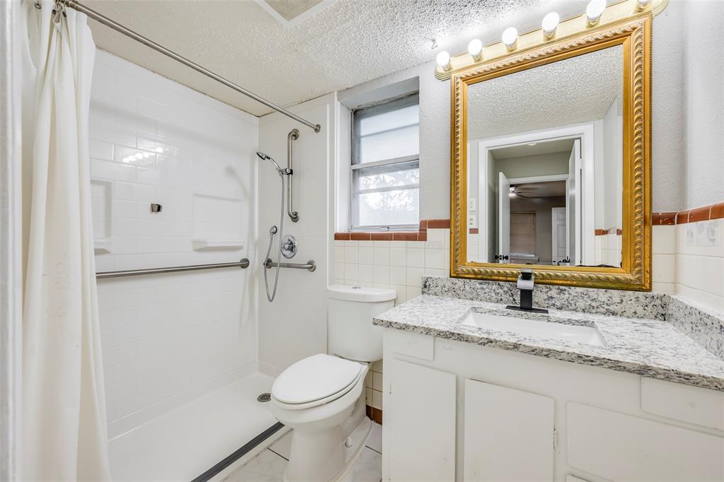 Bathroom featuring a stone-look countertop, integrated vanity, white tile shower surround, shower grab bars, and a hand-held shower fixture