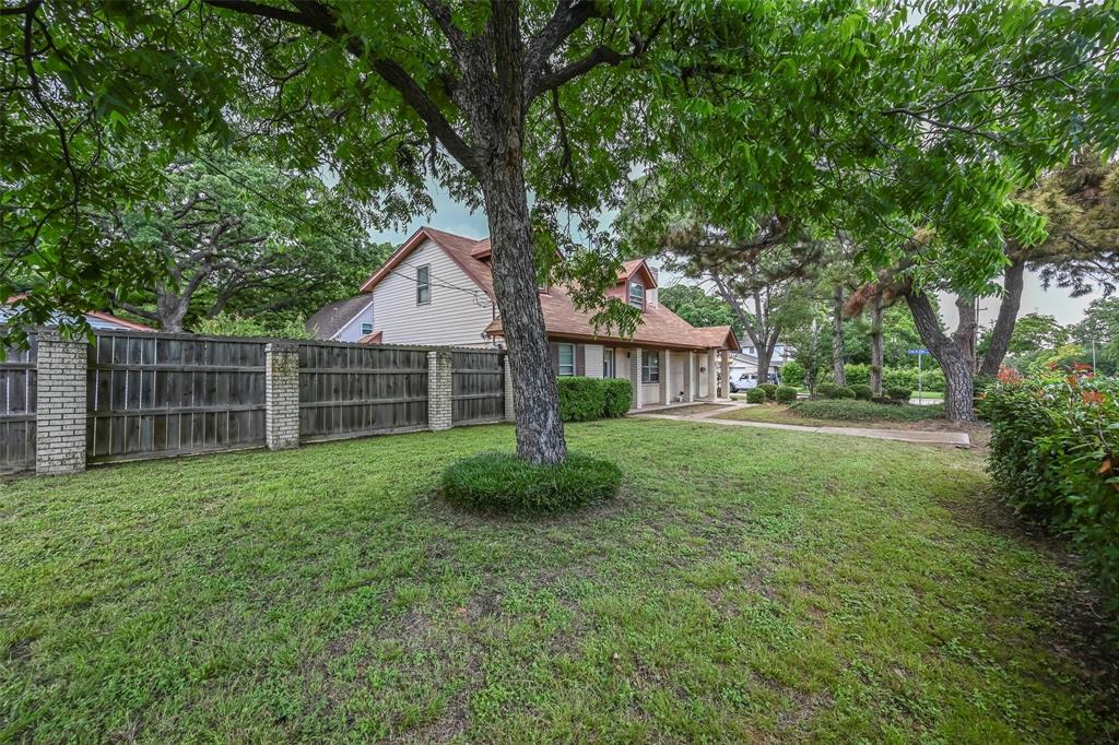 Expansive lawn area with mature trees, wood privacy fencing featuring brick support pillars, and concrete walkway