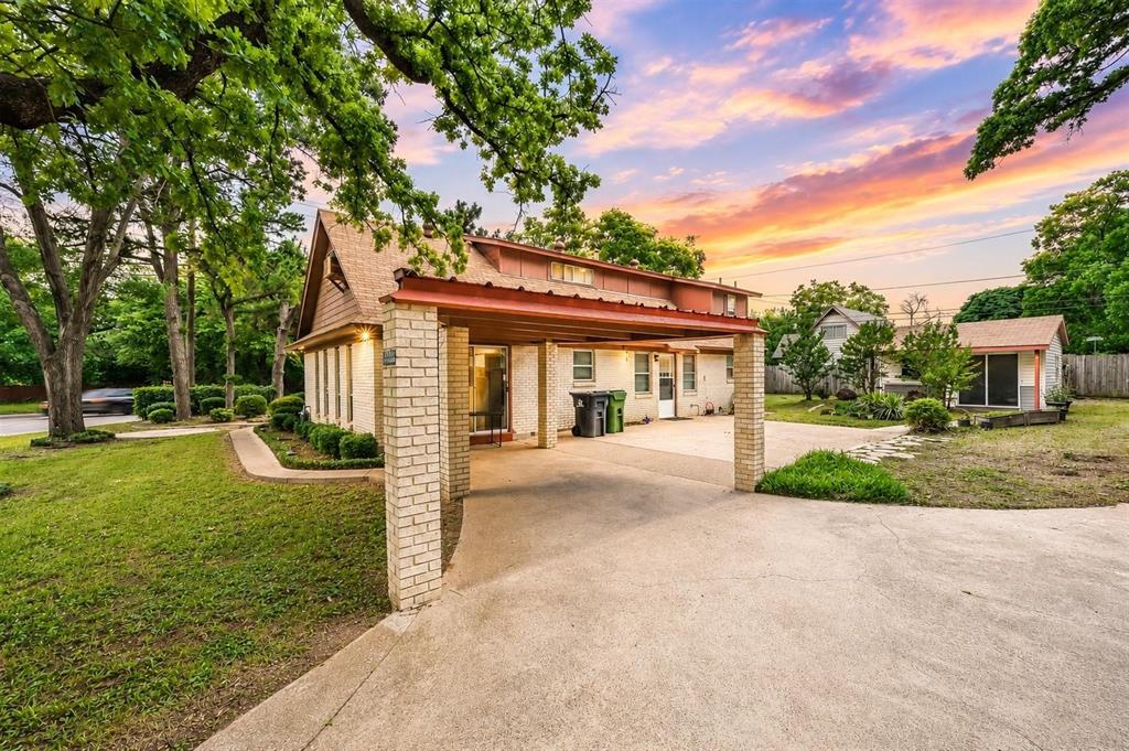 Brick exterior featuring a covered carport, concrete driveway, and detached storage structure situated on a lot with mature trees