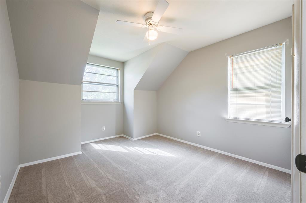 Room featuring slanted ceiling lines, neutral-toned wall paint, wall-to-wall carpeting, dual windows, and a central ceiling fan with an integrated light fixture