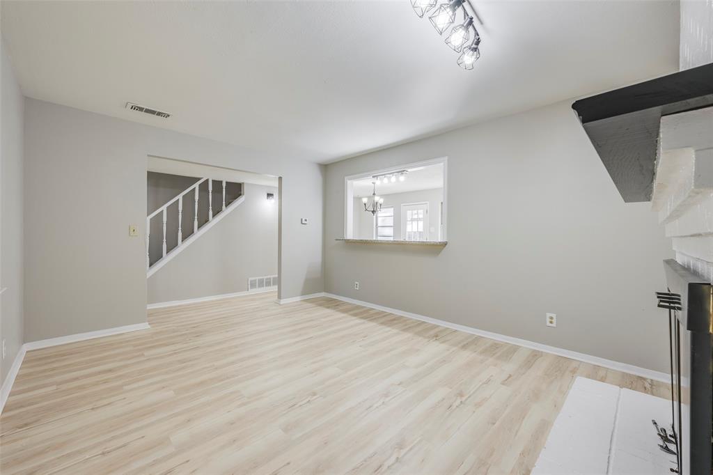 Living area featuring wood-finish flooring, a painted brick fireplace surround with a black mantel, a pass-through opening, and a staircase with a white railing