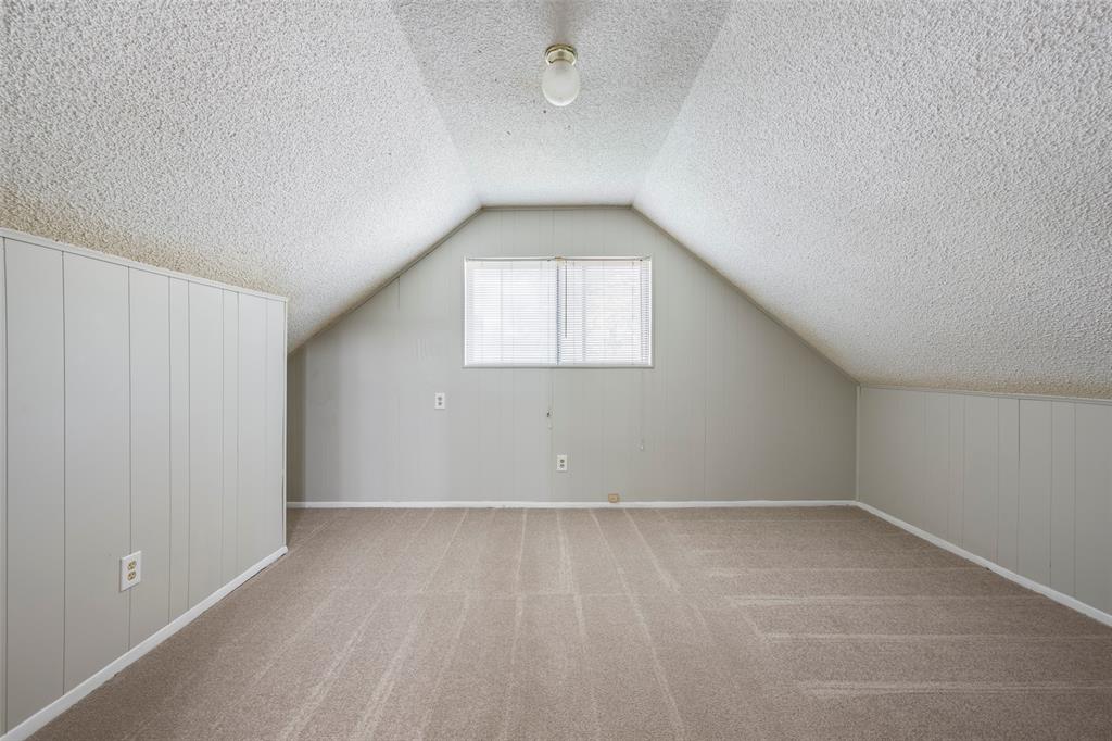 Sloped ceiling with textured finish, neutral carpeting, paneled wall detailing, and a central window providing natural light