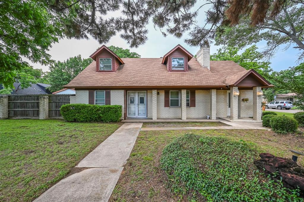 Traditional brick exterior featuring a covered front porch, dual dormer windows, a masonry chimney, and wood-paneled shutters