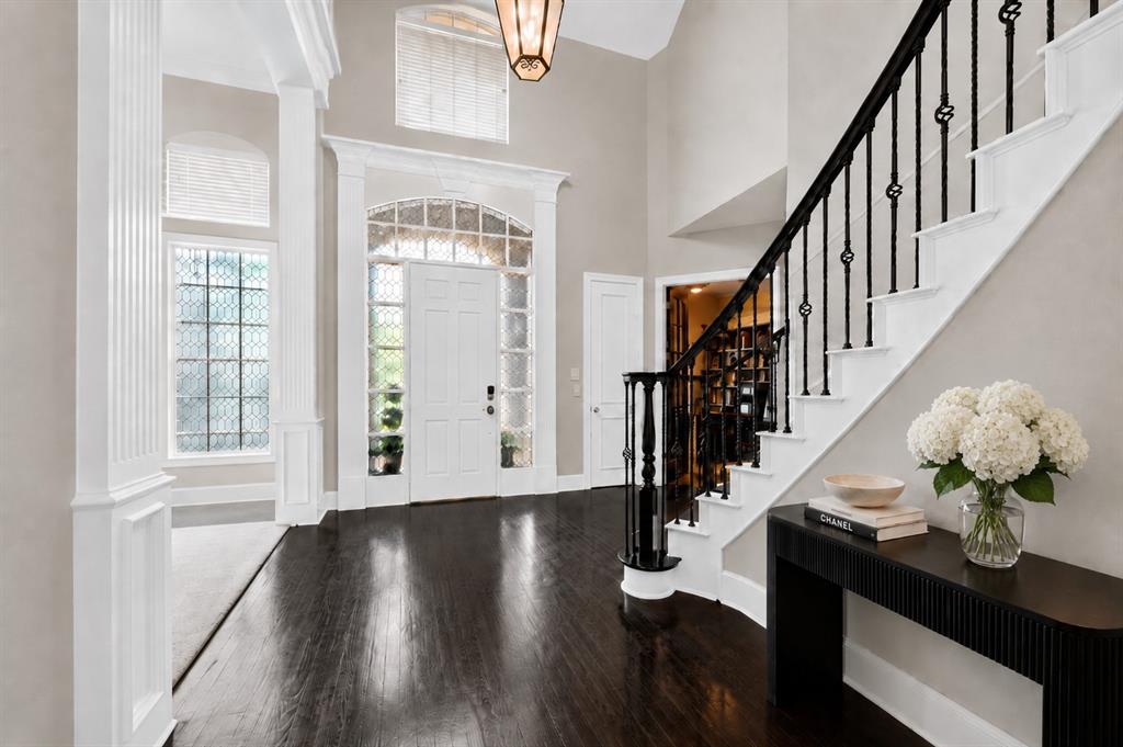 Grand foyer featuring high ceilings, wood-finish flooring, a decorative staircase with a black iron railing, and an arched entry door with sidelights and transom window