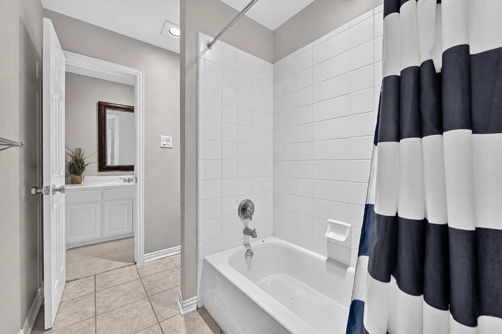 Full-height white tile shower surround, integrated tub, light-toned ceramic tile flooring, built-in white vanity cabinetry, and a wall-mounted rectangular mirror