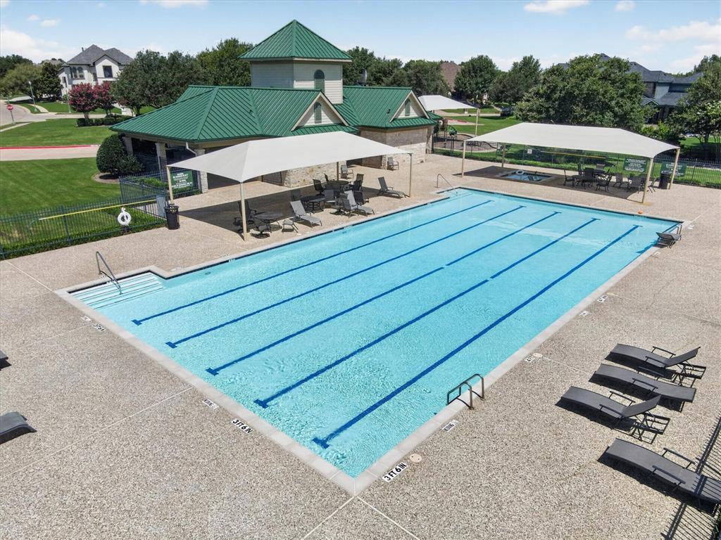 Lap-style swimming pool featuring aggregate decking, multiple shade structures, and an attached pavilion with a metal roof