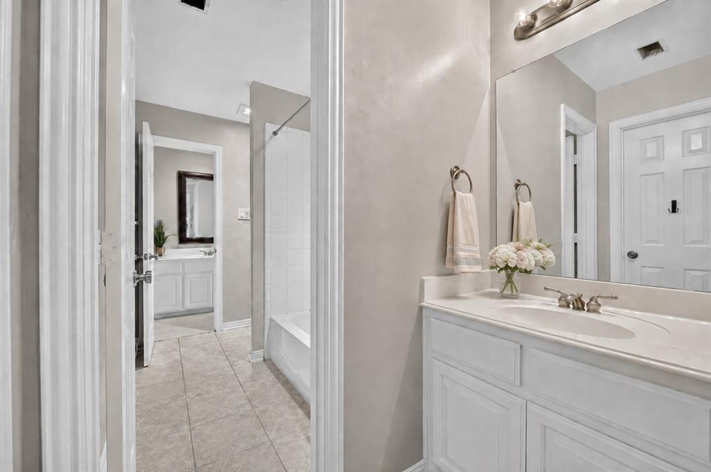 Bathroom featuring white cabinetry, an integrated sink with a polished metal faucet, a large wall-mounted mirror, and tile flooring