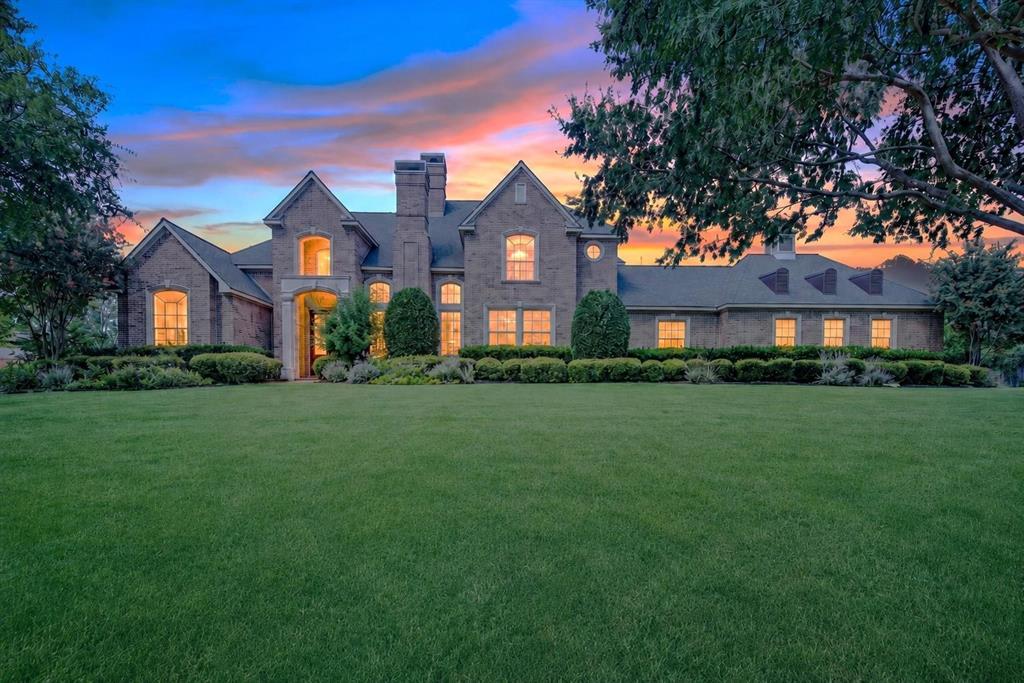 Traditional brick exterior featuring multiple gables, arched window detailing, a prominent chimney, and manicured landscaping