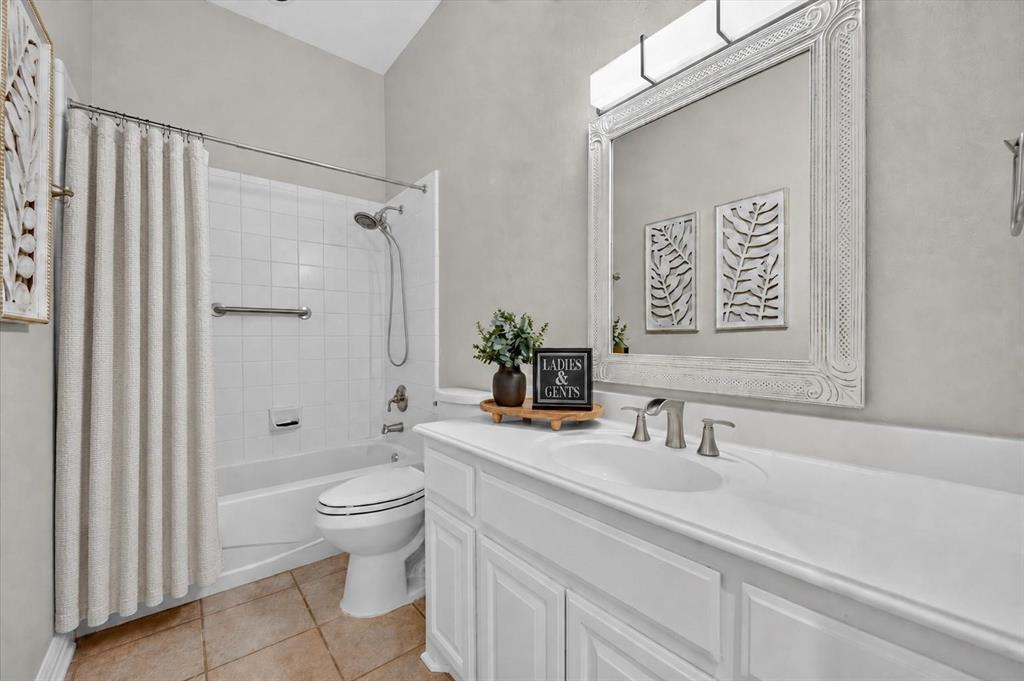 Bathroom featuring a white vanity cabinet with an integrated countertop, wall-mounted light fixture, decorative framed mirror, and a tub-shower combination with ceramic tile surround