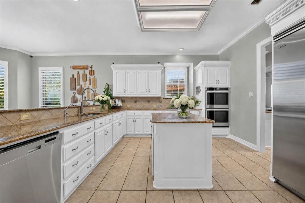 Kitchen featuring white cabinetry, stone-surface countertops, tile flooring, a center island, and stainless steel double wall ovens