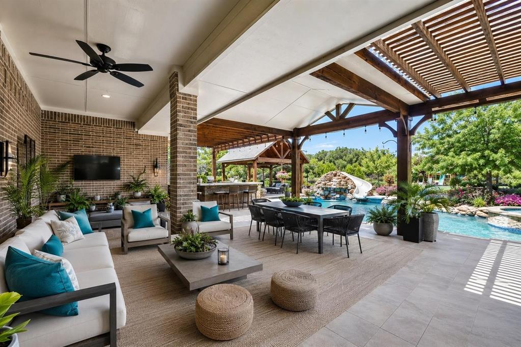 Covered patio featuring brick masonry, a wood-slat pergola, a ceiling fan, and tile flooring, opening to an outdoor kitchen and a swimming pool with a rock feature and slide