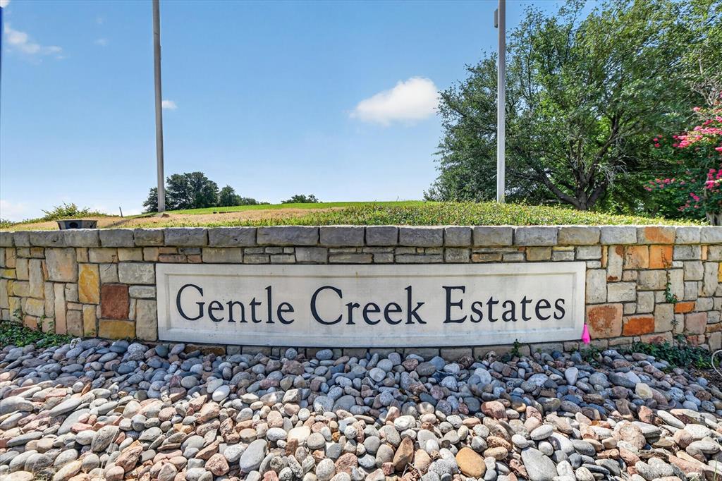 Stone masonry entrance monument featuring a smooth central stone inlay, tiered stacked-stone facade, and surrounding decorative river rock landscaping