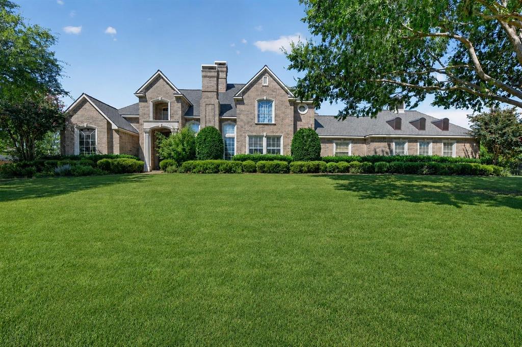 Brick exterior residence featuring a gabled roofline, central chimney, multi-pane windows, and extensive landscaping