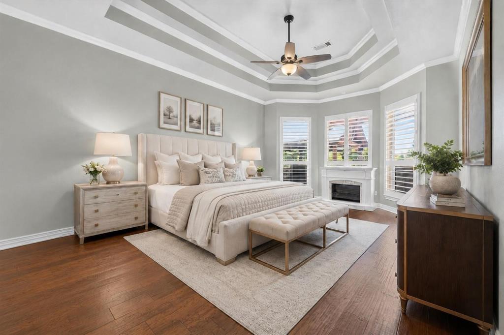 Tray ceiling with crown molding, wood-finish flooring, fireplace with a custom mantel, and windows equipped with plantation shutters
