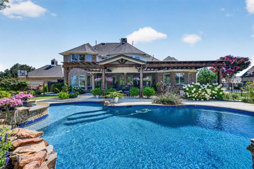 Brick exterior featuring a multi-level roofline, extensive covered pergola with timber framing, custom-shaped swimming pool, and stone masonry waterfall element