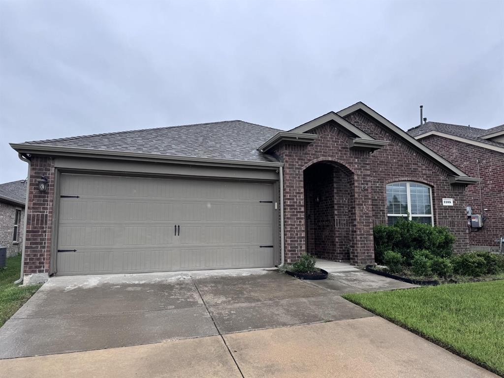 Brick exterior featuring an arched entryway, gabled roofline, concrete driveway, and a two-car garage