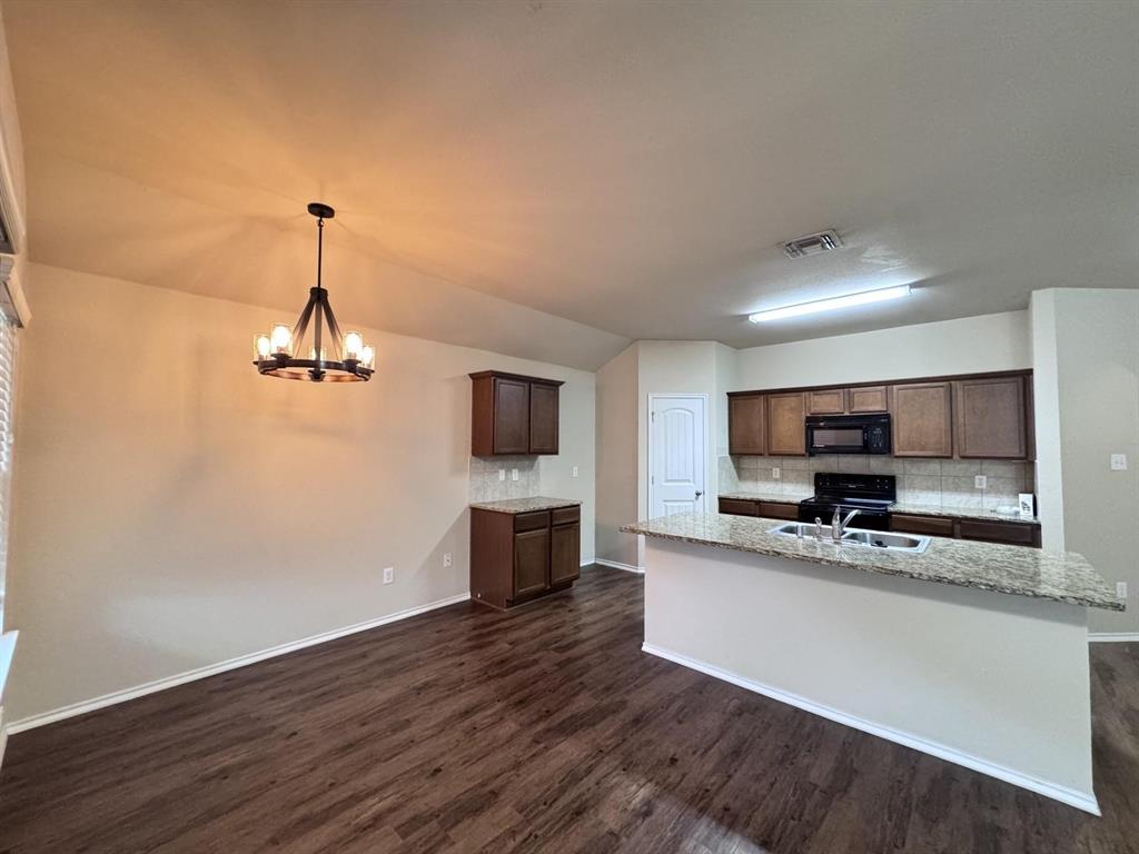 Kitchen featuring dark wood-finish cabinetry, stone-style countertops, wood-finish flooring, a stainless steel double-basin sink, and a multi-arm wagon wheel chandelier