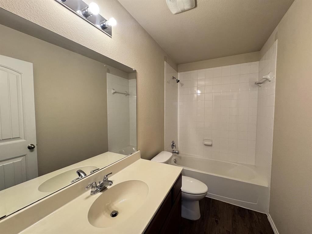 Bathroom featuring a vanity with integrated sink, expansive wall-mounted mirror, three-light overhead fixture, and a tub-shower combination with white tile surround