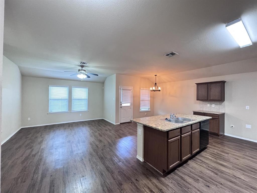 Open-concept interior featuring wood-finish flooring, a kitchen island with stone-finish countertops, dark wood-finish cabinetry, a vaulted ceiling with an integrated ceiling fan, and a multi-light chandelier