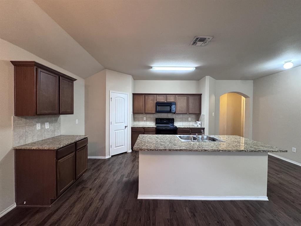 Kitchen featuring dark wood-finish cabinetry, stone-style countertops, a central island with an integrated dual-basin sink, and wood-finish flooring