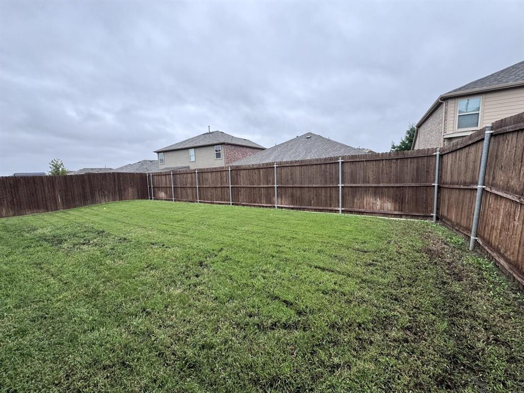 Backyard featuring a grass lawn enclosed by wood privacy fencing with metal posts