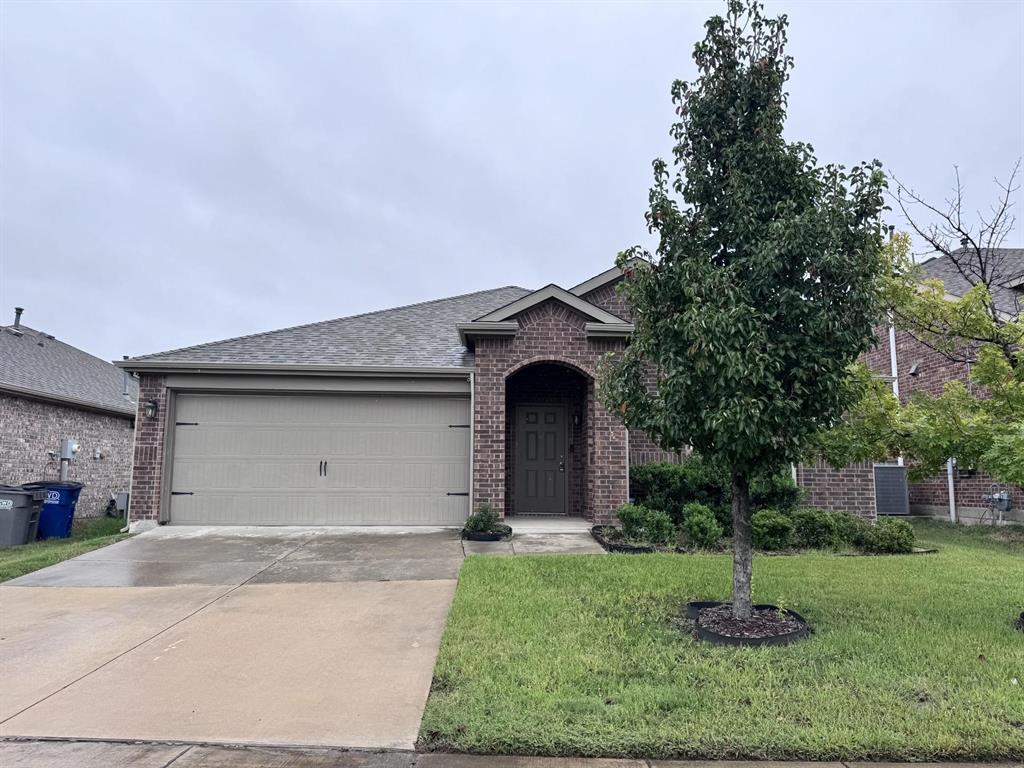 Brick exterior featuring a covered entryway, a front-facing attached garage, and a manicured lawn with ornamental landscaping