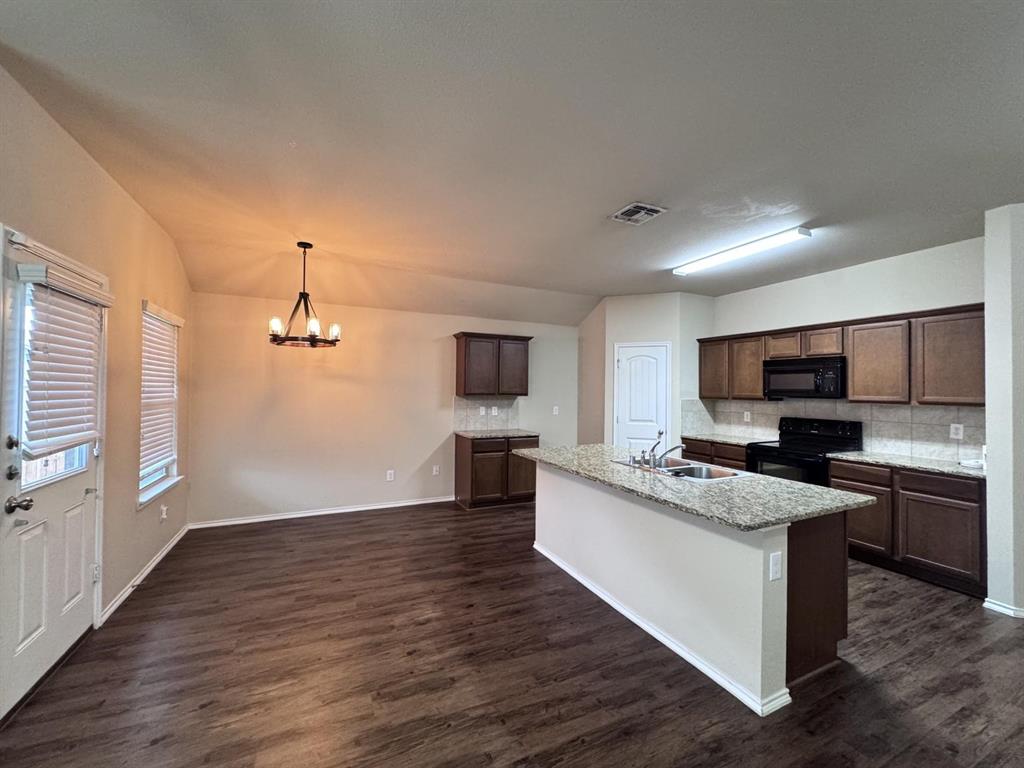 Kitchen featuring an island with a stone-surface countertop, dark-finish cabinetry, wood-finish flooring, and a multi-light chandelier