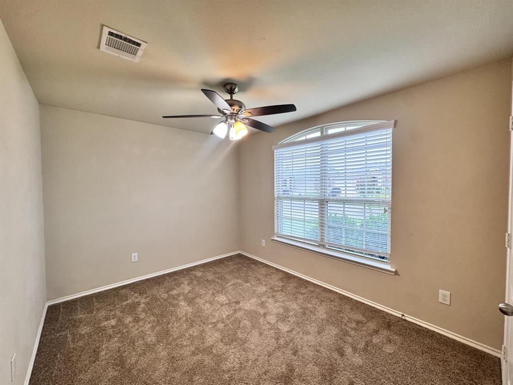 Neutral-toned room featuring plush carpeting, a multi-blade ceiling fan with integrated light fixture, and an arched window with horizontal blinds