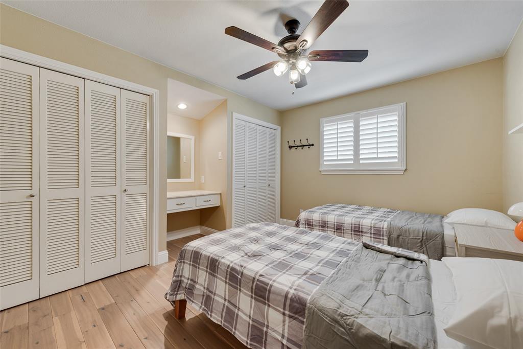 Wood-finish flooring, louvered closet doors, built-in vanity, ceiling fan with integrated lighting, and plantation shutters