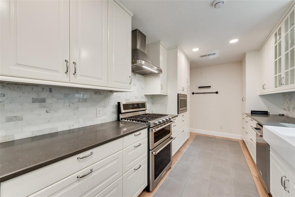 Kitchen featuring white shaker-style cabinetry, stainless steel double oven with gas cooktop, stone tile backsplash, contrasting dark countertops, and large-format porcelain tile flooring