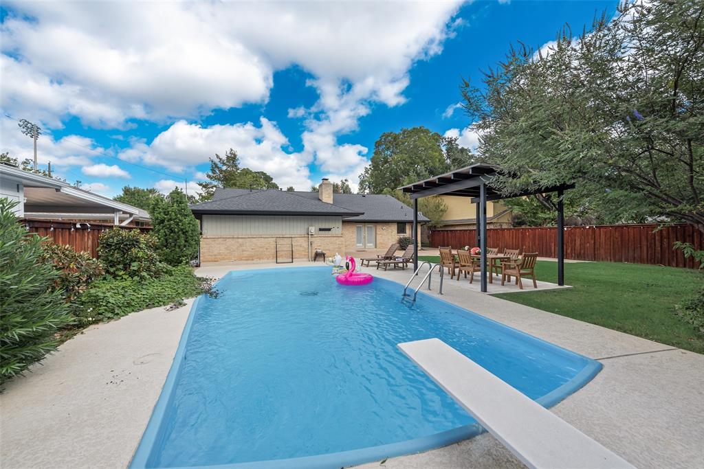 In-ground swimming pool with a diving board, concrete patio, detached dark-finish pergola, and wood-panel perimeter fencing