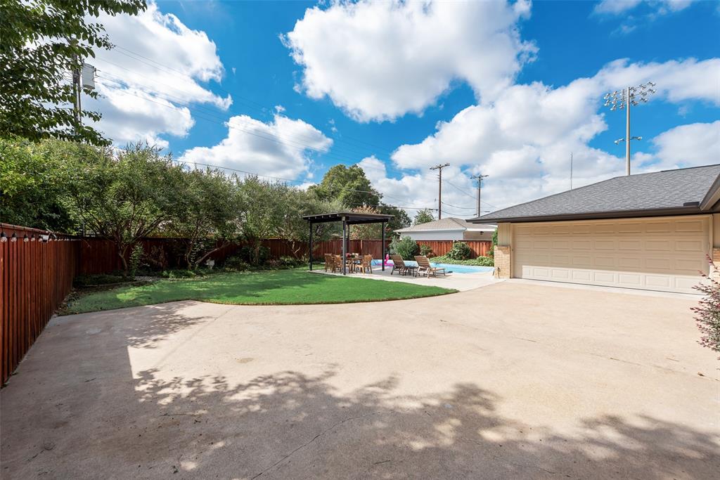 Backyard featuring a concrete driveway, grass lawn, swimming pool, wood privacy fencing, and a detached pergola