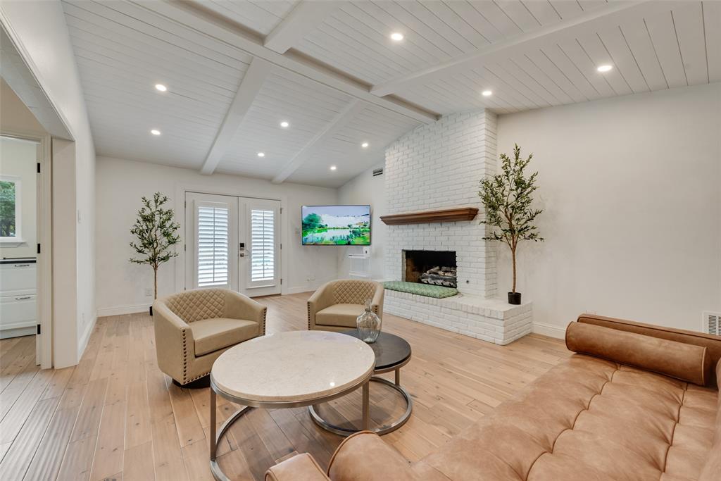 Living area featuring a vaulted ceiling with exposed beams, white brick fireplace, wood-finish flooring, recessed lighting, and glass-paneled double doors