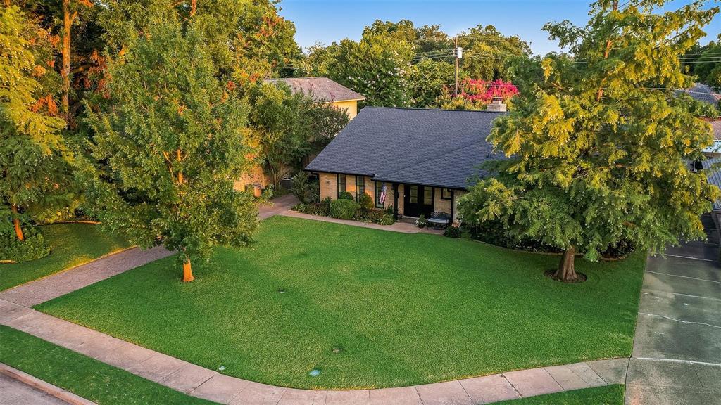 Single-story residence featuring a pitched roof, expansive front lawn, mature trees, and a paved driveway Single-story residence featuring a pitched roof, expansive front lawn, mature trees, and a paved driveway