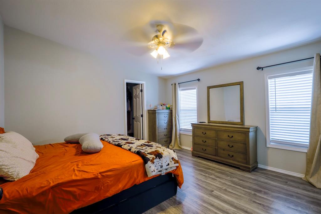 Bedroom featuring wood-finish flooring, dual windows with horizontal blinds, and a central ceiling fan with integrated lighting