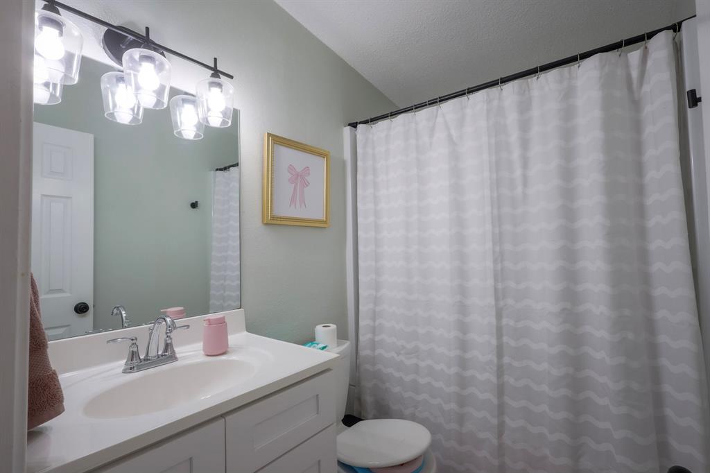 White vanity cabinet with an integrated sink, polished metal faucet, large rectangular mirror, and four-light glass vanity fixture