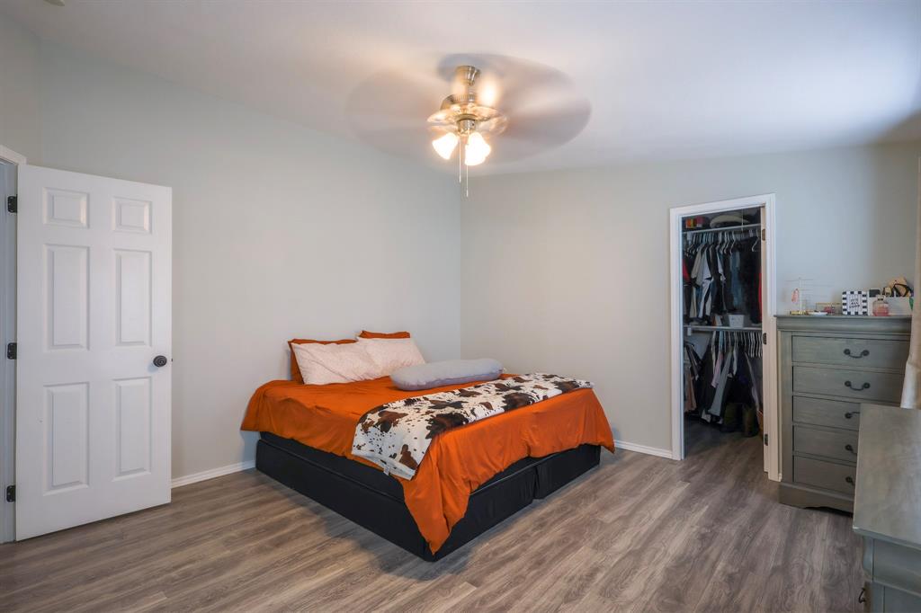 Neutral-toned walls, wood-finish flooring, overhead ceiling fan with integrated lighting, and a walk-in closet with built-in shelving