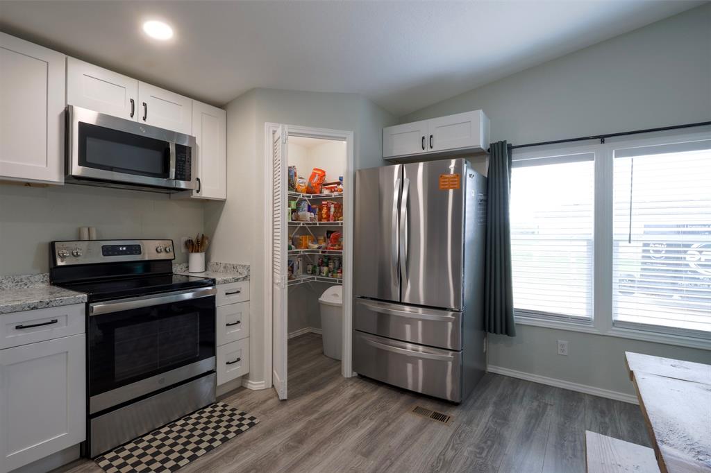 Kitchen featuring white shaker-style cabinetry, stainless steel appliances, speckled countertops, wood-finish flooring, and a walk-in pantry with wire shelving