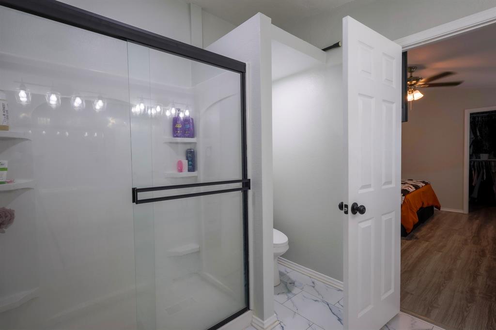 Walk-in shower with matte black sliding glass doors, integrated shelving, and white tile flooring with gray veining