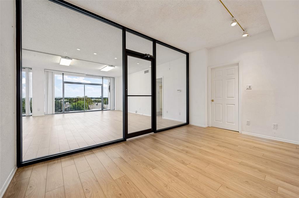 Floor-to-ceiling glass partition with black metal framing, wood-finish flooring, adjustable track lighting, and expansive glass sliding doors