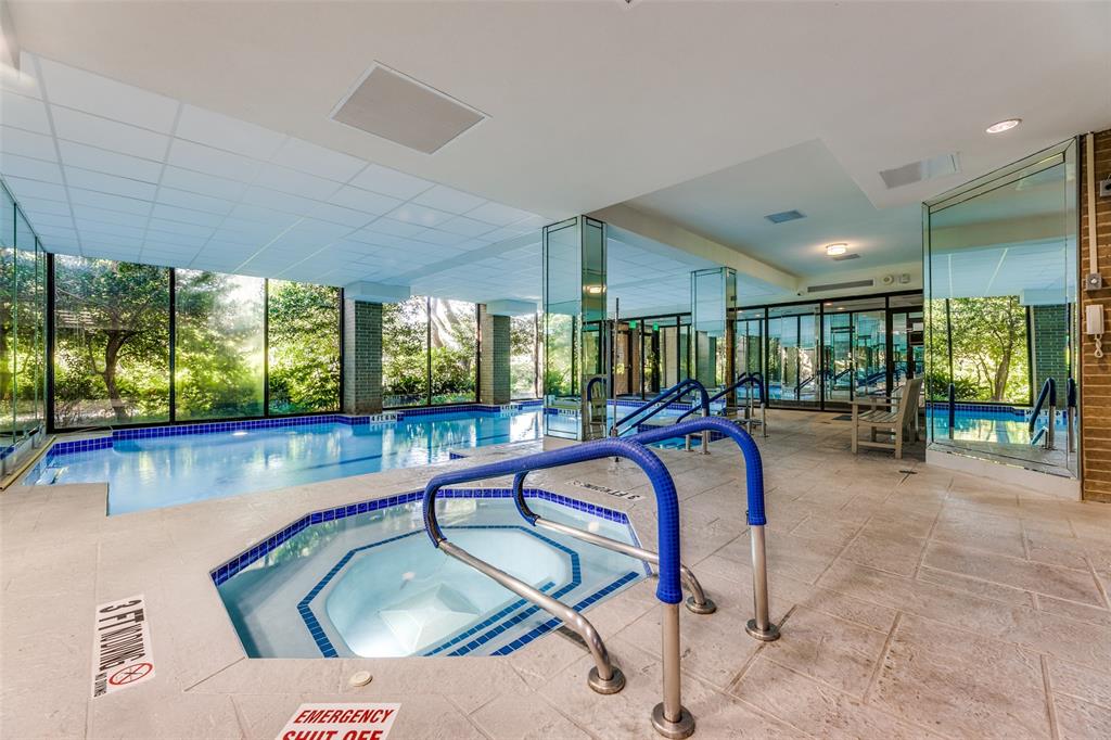 Indoor aquatic center featuring a heated lap pool, an integrated jetted spa, floor-to-ceiling glass paneling, and stone-tile flooring