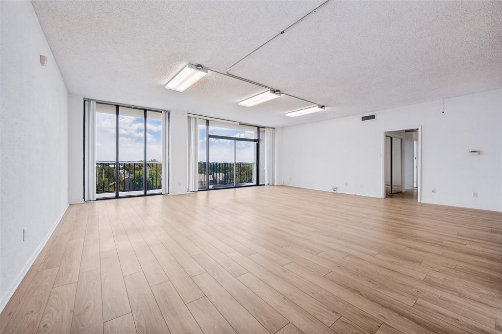 Spacious room featuring wood-finish flooring, floor-to-ceiling glass sliding doors, and industrial-style surface-mounted lighting