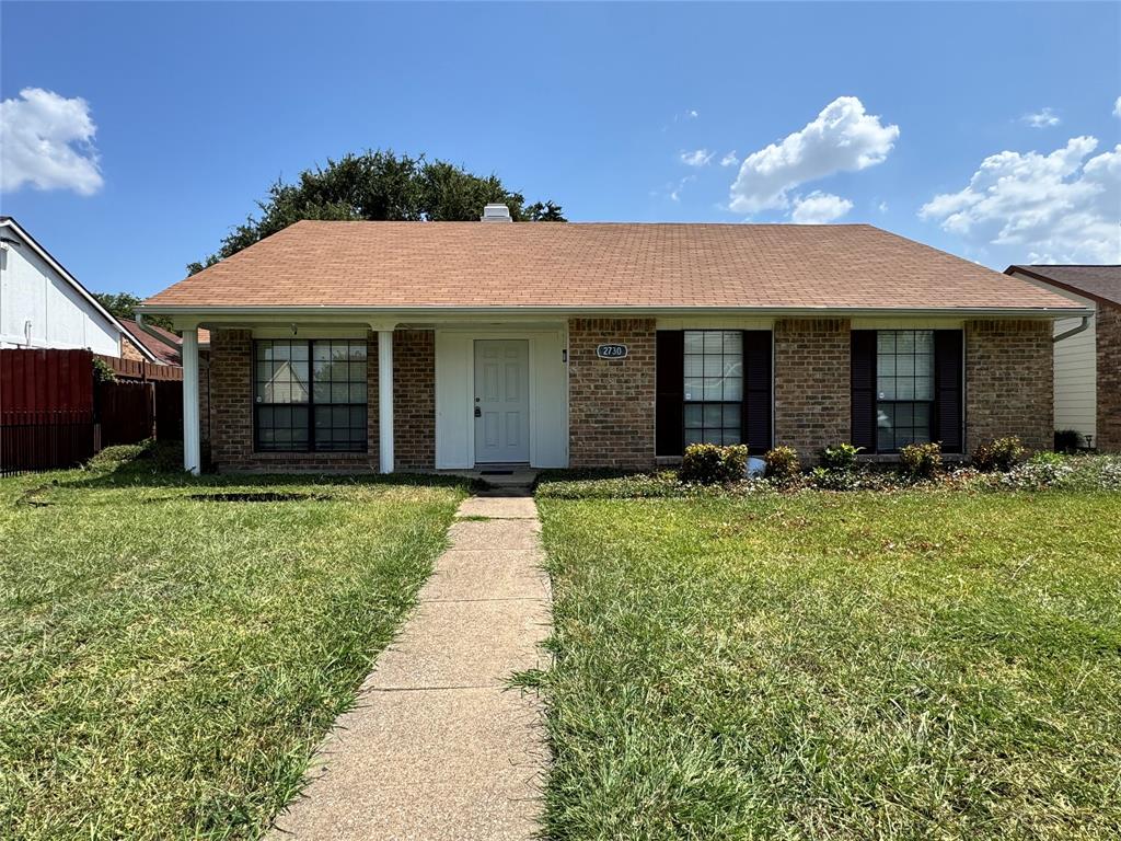 Single-story brick exterior featuring a covered front porch, asphalt shingle roof, dark window shutters, and a concrete walkway