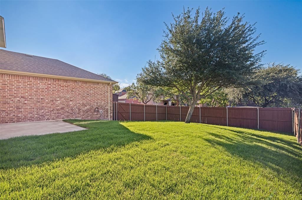 Backyard featuring a brick exterior wall, a concrete patio, a mature tree, and a solid wood-tone privacy fence