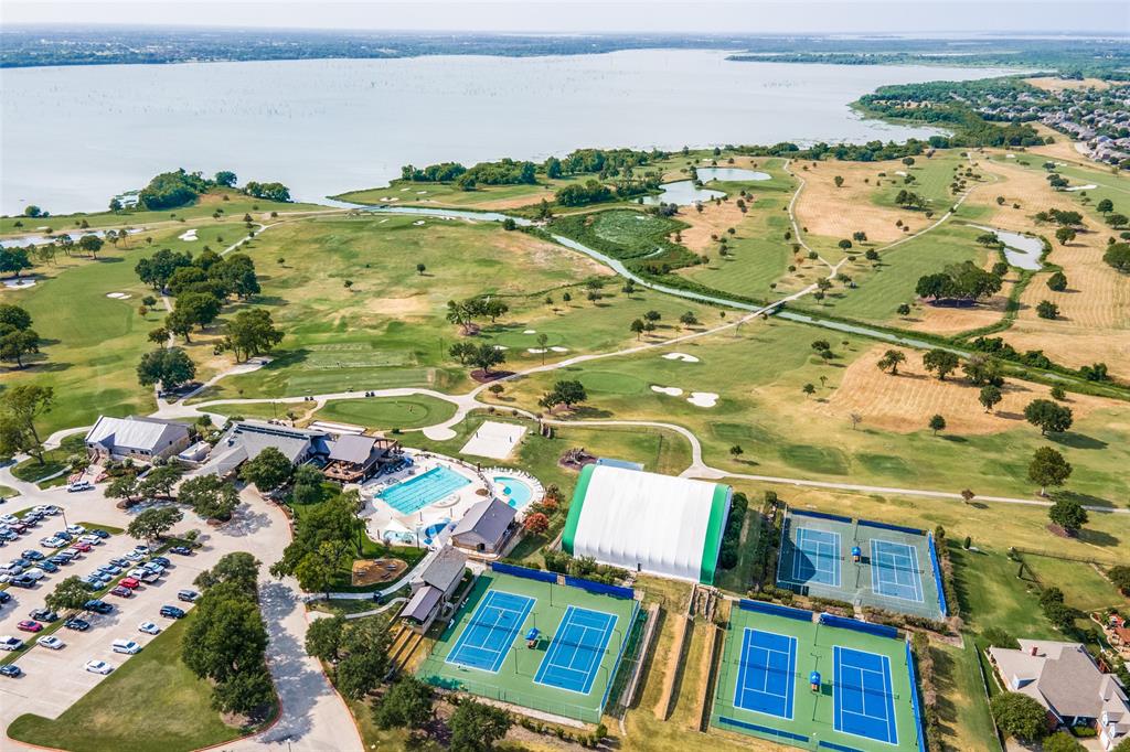 Aerial perspective of a multi-purpose recreational complex featuring multiple tennis courts, a swimming pool, a covered sports structure, and expansive green space bordering a large lake