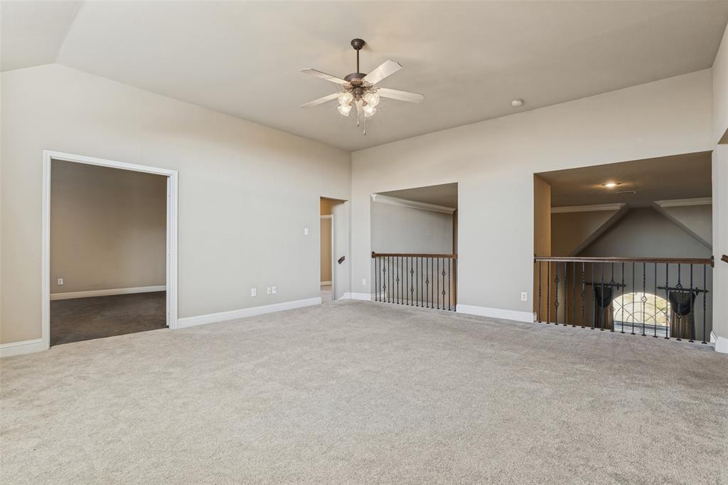 Vaulted ceilings, carpeted flooring, multi-blade ceiling fan with integrated lighting, and decorative metal baluster railings