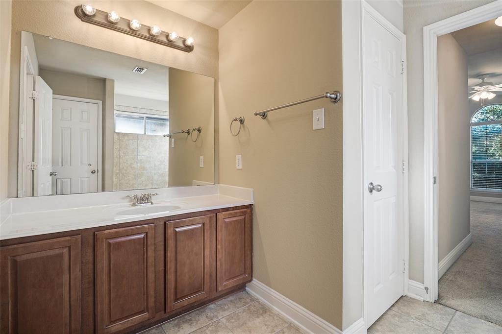 Bathroom vanity featuring wood cabinetry, solid-surface countertop with an integrated sink, full-width wall mirror, and multi-bulb vanity light fixture